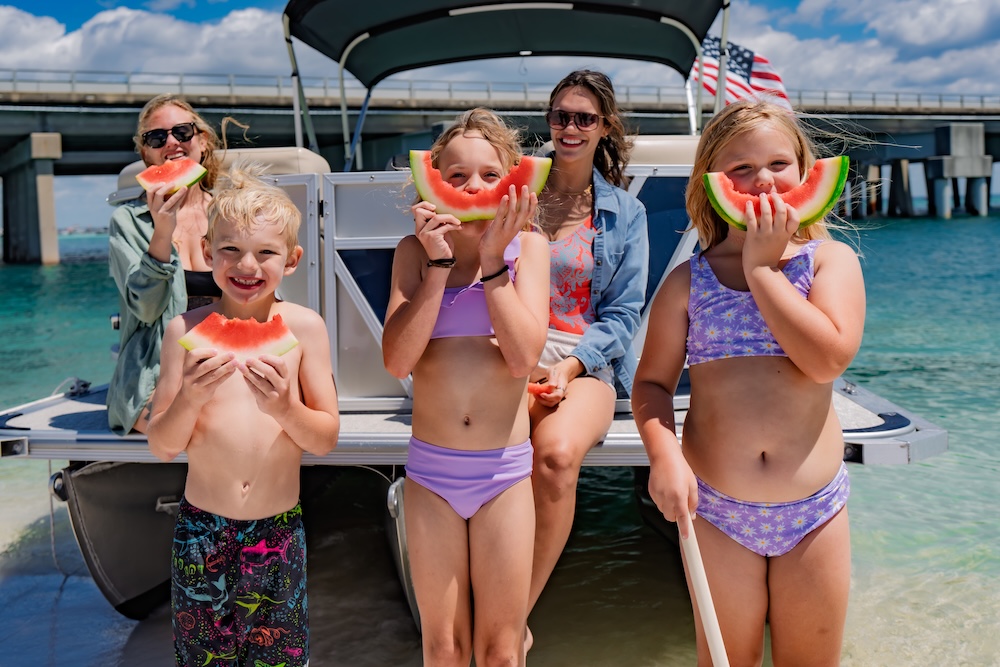 family eating and posing with watermelon in front of tritoon at destin fl beach