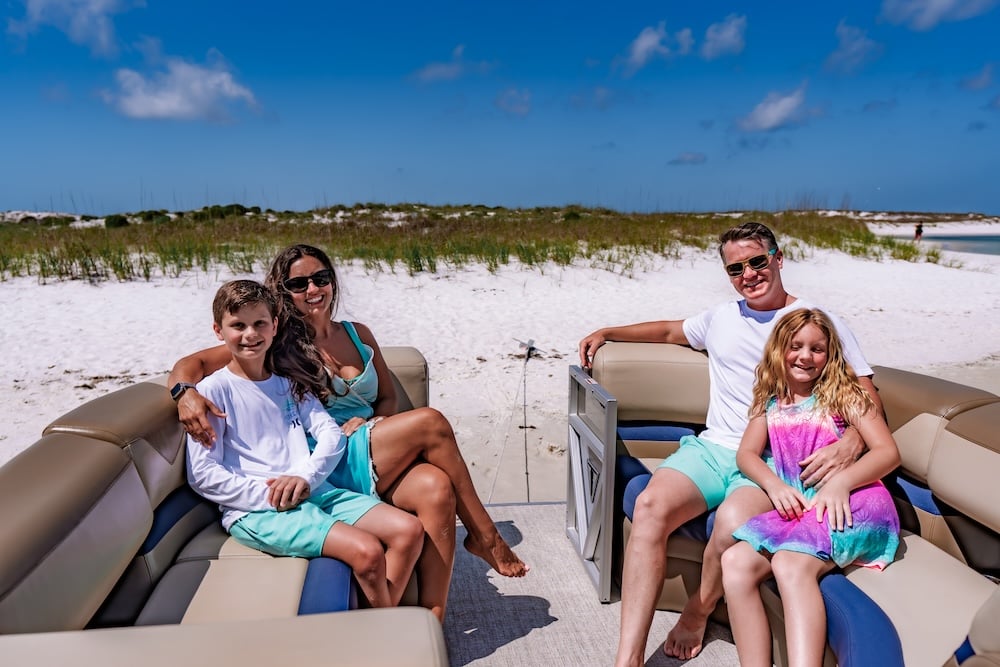family of four smiling for the camera on a tritoon boat at shell island in panama city beach
