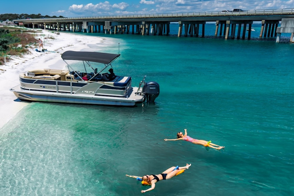 two women floating beside beached tritoon in destin fl