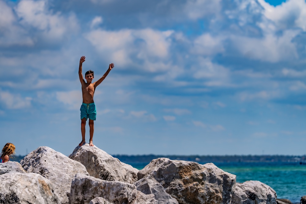 young boy waving to camera from rock wall at shell island in panama city beach